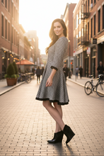 Load image into Gallery viewer, Woman in a black and white checkered dress standing on a city street.
