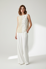 Load image into Gallery viewer, A woman models a sleeveless color-block top with cream and white lace panels, paired with white wide-leg trousers, against a bright, minimalist studio background.
