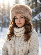 Įkelti nuotrauką į galerijos peržiūros programą, A woman wearing a beige faux fur hat and a cream cable-knit sweater, standing in a snowy outdoor setting.
