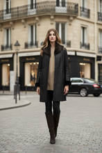 Load image into Gallery viewer, A woman stands on a cobblestone city street wearing a black mid-length coat with dark brown fur trim, a beige sweater, black leggings, and tall brown boots. Parisian-style buildings and a blurred car are in the background.
