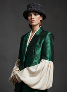 Model wearing a green brocade jacket with a white garment underneath against a dark background