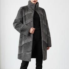 Įkelti nuotrauką į galerijos peržiūros programą, A model stands in a minimalist studio wearing a long, high-neck, textured gray coat over a black dress and black boots.
