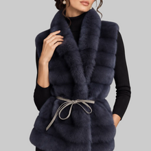 Load image into Gallery viewer, A woman models a dark navy blue fur vest with a gray tie belt over a black top, set against a neutral gray studio background.
