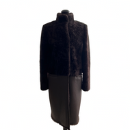 A chocolate brown knee-length sheepskin fur coat with astrakhan (karakul) fur decoration, displayed on a mannequin. It features a stand turtleneck collar, press-stud fastening, and front pockets.