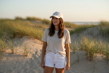 Load image into Gallery viewer, Woman standing on a sandy beach with grasses and a clear sky

