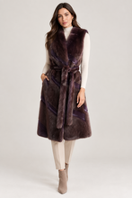 Įkelti nuotrauką į galerijos peržiūros programą, A woman models a long, sleeveless plush faux-fur vest in a deep plum purple color, styled over a cream turtleneck, beige trousers, and taupe ankle boots against a light gray studio background.
