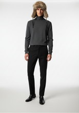 Load image into Gallery viewer, A male model stands against a white studio background wearing a dark gray knit turtleneck sweater, black trousers, black leather boots, and a brown fur trapper hat with ear flaps.
