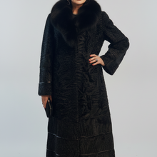 Įkelti nuotrauką į galerijos peržiūros programą, An older woman stands against a light gray studio background wearing a long black textured coat with a large dark fur collar and holding a small black clutch.
