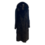 Black long astrakhan fur coat with fox fur collar, with hidden pockets in front and decorative leather details at then end.