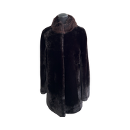 A long black sheepskin fur coat with a pink silver fox fur collar, displayed on a mannequin.