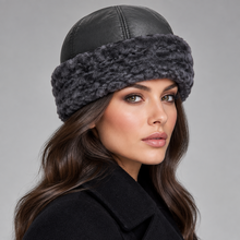 Load image into Gallery viewer, A woman wearing a black faux-leather winter hat with a thick, dark gray fuzzy trim, shown in a close-up profile against a neutral gray background.
