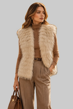 Load image into Gallery viewer, A woman models a sleeveless beige faux fur vest over a brown turtleneck, paired with brown wide-leg trousers and holding a brown handbag, set against a solid gray studio background.
