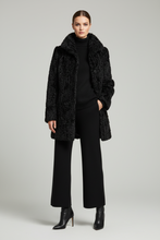 Load image into Gallery viewer, A model stands against a light gray studio background wearing a black textured faux-fur coat over a black ribbed turtleneck, black wide-leg pants, and black heeled ankle boots.
