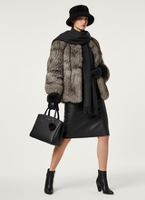 Įkelti nuotrauką į galerijos peržiūros programą, A model is shown wearing a luxurious winter outfit consisting of a gray and black fur jacket, a black scarf, a black leather skirt, black gloves, black ankle boots, and a black bucket hat. She is holding a black leather handbag with a pom-pom against a plain light gray studio background.
