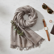 Gray patterned scarf with sunglasses, watch, and wallet on a light surface