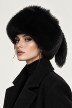 Įkelti nuotrauką į galerijos peržiūros programą, A close-up portrait of a model wearing a luxurious black fur ushanka hat and a matching black coat against a light off-white background.
