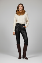 Load image into Gallery viewer, A model stands against a light gray studio background wearing a cream cable-knit sweater with a brown faux-fur collar, black faux-leather pants, a black belt, and dark brown knee-high boots.
