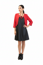 Įkelti nuotrauką į galerijos peržiūros programą, A woman modeling a red cropped jacket over a black slip dress, accessorized with a large red circular pendant necklace and black ankle boots, against a plain white background.
