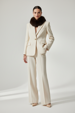 Įkelti nuotrauką į galerijos peržiūros programą, A model stands in a studio wearing a structured cream-colored two-piece suit with wide-leg trousers and a dark brown fur collar, paired with beige pointed-toe heels.
