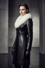 Įkelti nuotrauką į galerijos peržiūros programą, A woman wearing a black leather coat with a large white fur collar, black gloves, and black trousers, standing in a dark, minimalist interior with concrete pillars.
