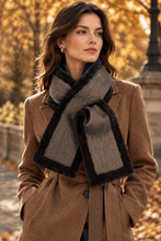 Įkelti nuotrauką į galerijos peržiūros programą, A woman outdoors wearing a camel brown coat and a gray scarf with black faux-fur trim, set against a warm, blurred autumn background.
