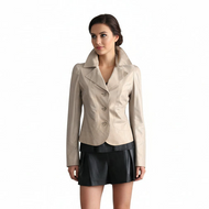 Woman wearing a beige blazer and black leather shorts standing on a patterned bag against a white background
