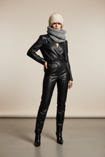 Load image into Gallery viewer, A model stands in a studio wearing a black faux-leather blazer and matching slim-fit pants, styled with a gray knit scarf, a cream knit beanie, and black ankle boots against a plain beige backdrop.
