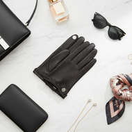Black leather gloves with a black handbag, sunglasses, wallet, and scarf on a light surface.