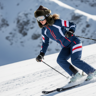 Person skiing down a snowy slope wearing a blue and red ski suit.