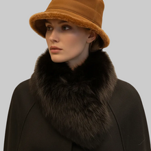 Įkelti nuotrauką į galerijos peržiūros programą, A close-up portrait of a model wearing a warm camel bucket hat with a fuzzy brown trim and a large dark brown fur collar over a black coat, set against a solid beige background.

