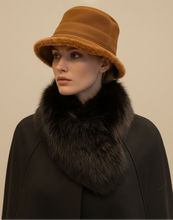 Įkelti nuotrauką į galerijos peržiūros programą, A model wearing a tan leather bucket hat with a brown faux-fur trim, paired with a black coat featuring a large dark brown fur collar, set against a solid beige background.
