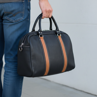 Person holding a black duffel bag with brown stripes against a neutral background