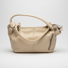 Įkelti nuotrauką į galerijos peržiūros programą, A light beige pebbled leather handbag with a single top handle, a side buckle detail, and a zippered pocket on the front, shown against a neutral light gray background.
