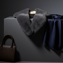 Įkelti nuotrauką į galerijos peržiūros programą, A dark gray fur collar draped over a hanger, styled with a navy blue satin fabric and a brown leather handbag on a dark gray pedestal against a dark background.
