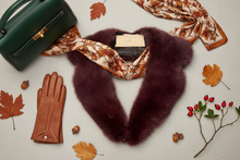 Įkelti nuotrauką į galerijos peržiūros programą, A styled flat-lay featuring a deep burgundy faux fur collar, a cream and brown patterned silk scarf, a dark green leather handbag, and a pair of brown leather gloves, arranged with autumn leaves, acorns, and berries on a light beige fabric background.
