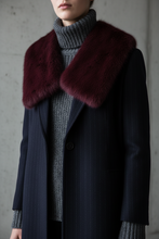 Įkelti nuotrauką į galerijos peržiūros programą, A close-up of a person wearing a dark navy pinstripe coat with a large deep burgundy fur collar over a gray ribbed turtleneck sweater.
