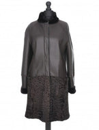 A chocolate brown knee-length sheepskin coat with astrakhan fur decoration, featuring a stand turtleneck collar, press-stud fastening, and front pockets. The coat is displayed on a mannequin.
